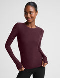 A woman modeling a long-sleeve crewneck top in a deep burgundy color, paired with black pants, against a solid light gray background.