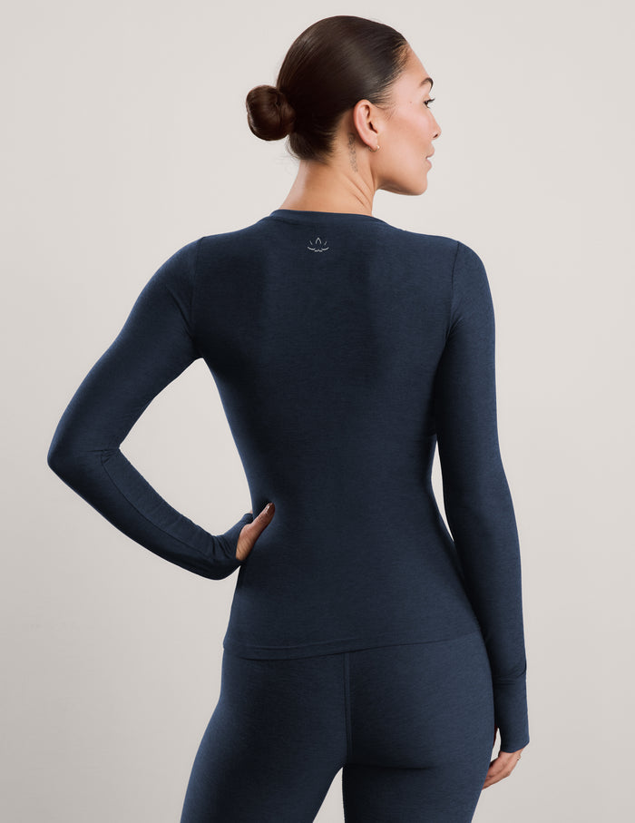 A woman modeling a dark navy blue long-sleeve crewneck top and matching leggings against a plain light gray studio background.