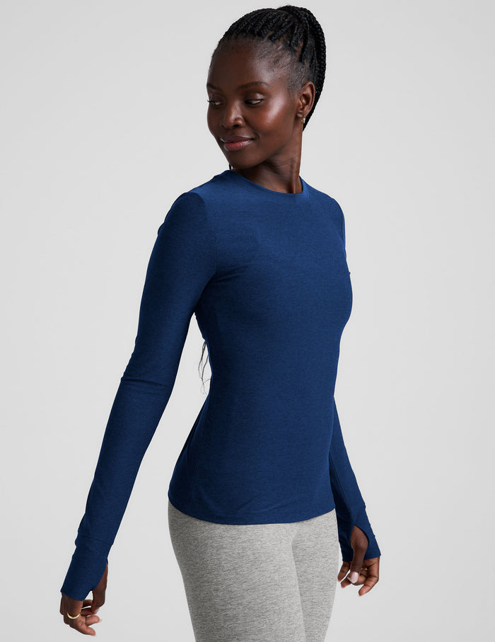 Woman wearing a blue long-sleeve top and gray leggings on a light gray background.