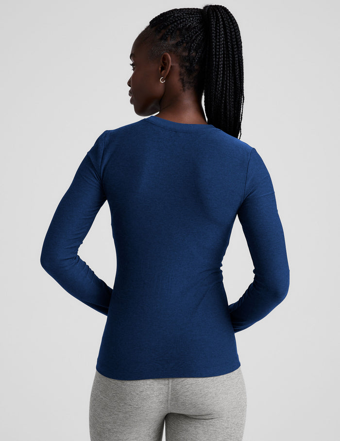 Woman wearing a blue long-sleeve top and gray leggings on a light gray background.