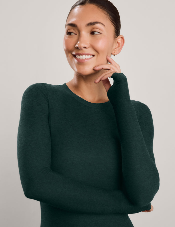 A woman modeling a dark forest green long-sleeve crewneck top and matching pants against a neutral light gray studio background.