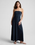 Woman wearing a strapless navy blue maxi dress on a light gray background.
