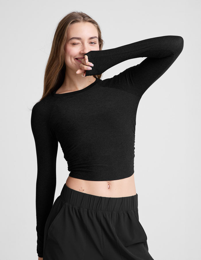 Woman wearing a black long-sleeve top and black pants on a light gray background.
