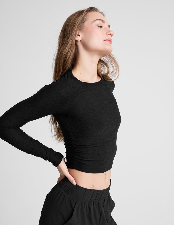 Woman wearing a black long-sleeve top and black pants on a light gray background.