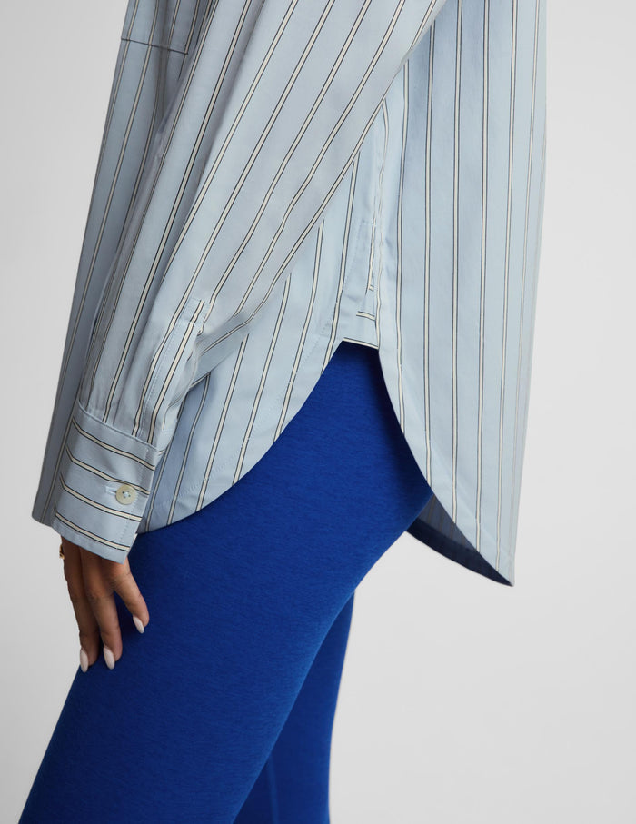 A close-up of a person wearing a light blue and white vertically striped button-up shirt with blue leggings, shown from the side against a plain light gray background.