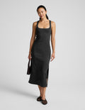 Woman wearing a black square neck midi length dress against a plain background.