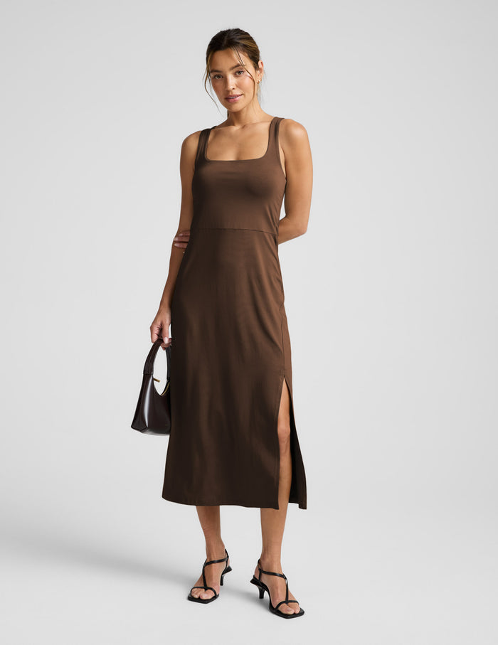 Woman wearing a brown square neck midi length dress against a plain background.