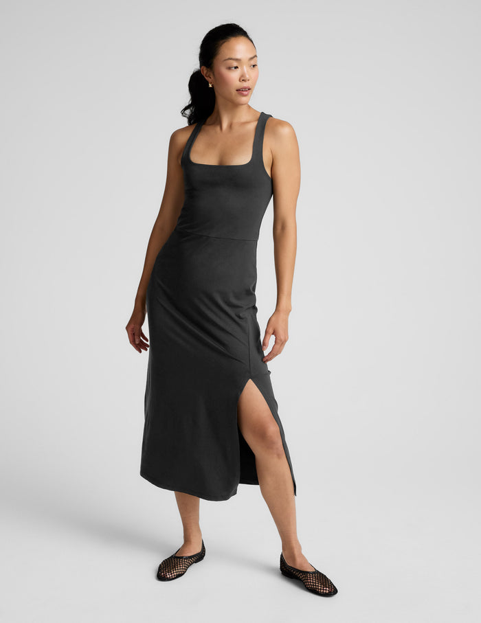 Woman wearing a black square neck midi length dress against a plain background.