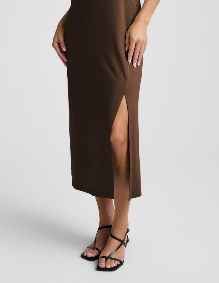 Woman wearing a brown square neck midi length dress against a plain background.