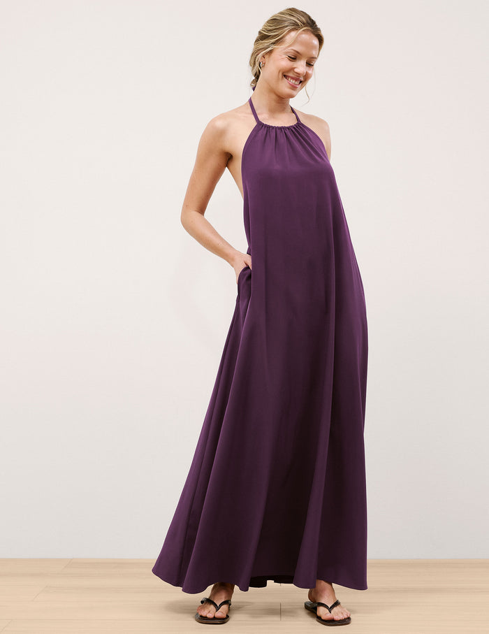 Woman wearing a purple halter neck maxi dress on a plain background.