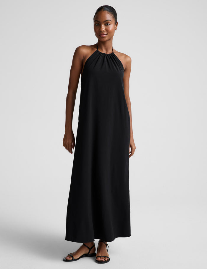 Woman wearing a black halter neck dress on a plain background.