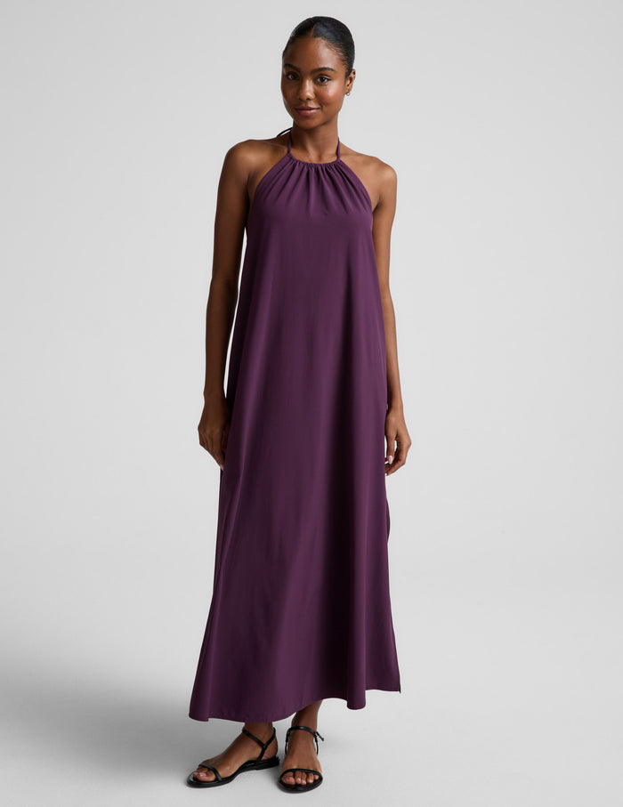 Woman wearing a purple halter neck maxi dress on a plain background.