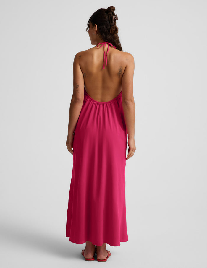 Woman wearing a red halter maxi dress with an open back against a light gray background.