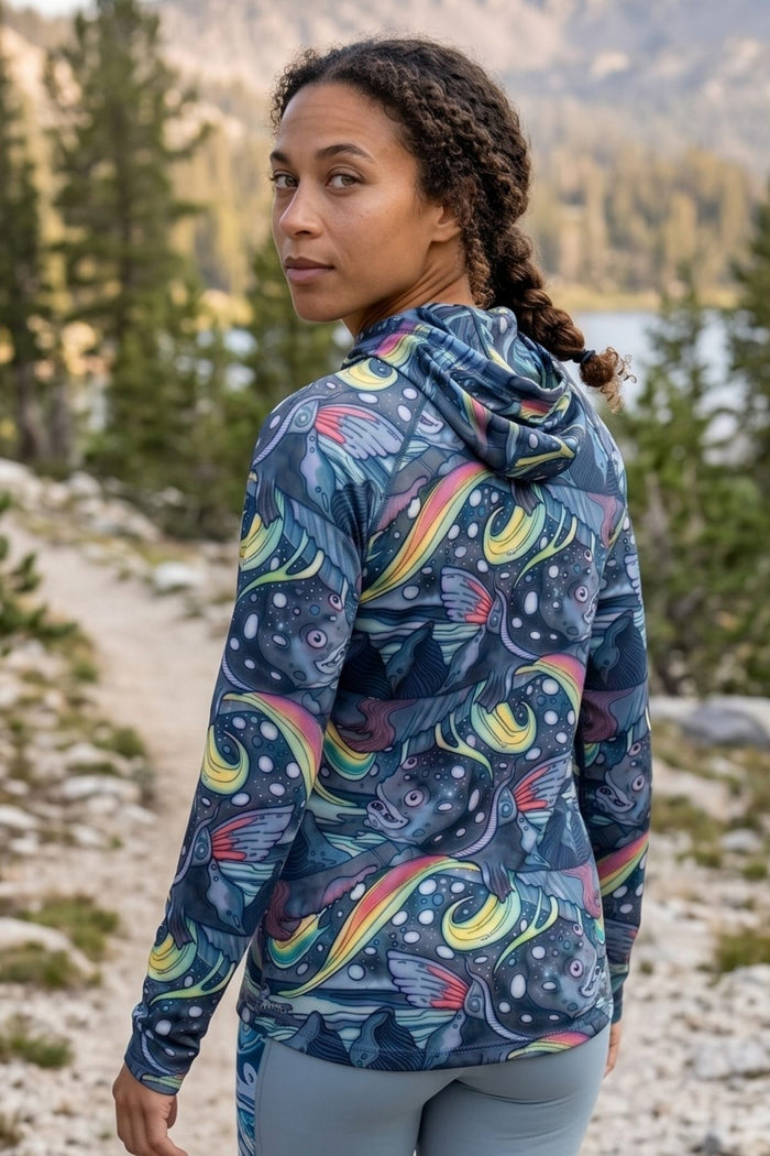 Woman wearing a colorful patterned jacket in a natural setting with trees and water.