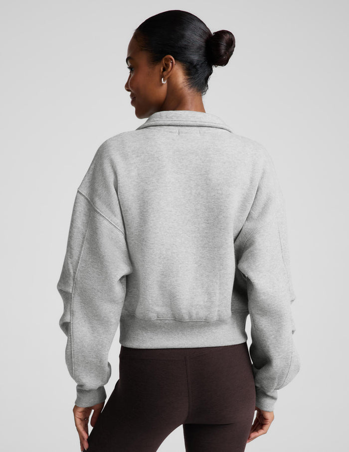A woman modeling a light gray zip-up fleece jacket and dark brown capri leggings against a light gray studio background.