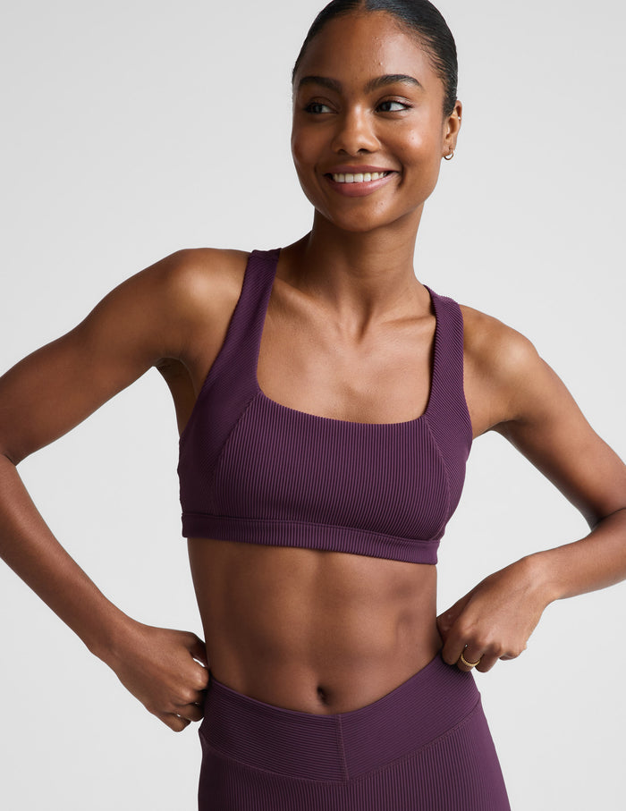Woman wearing a purple ribbed bra and leggings against a plain background.