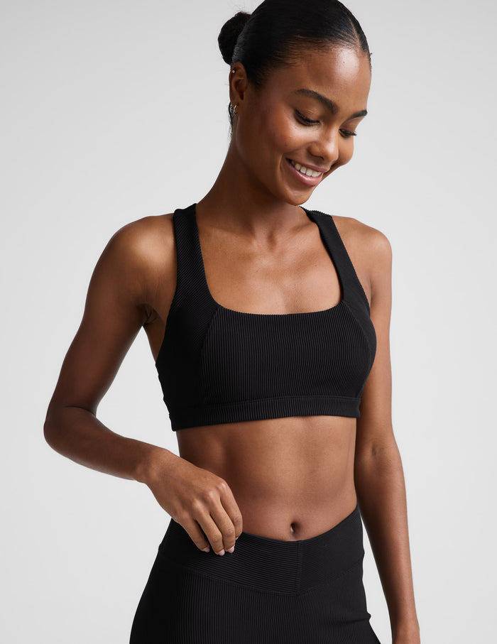 Woman wearing a black ribbed bra and black leggings against a plain background.
