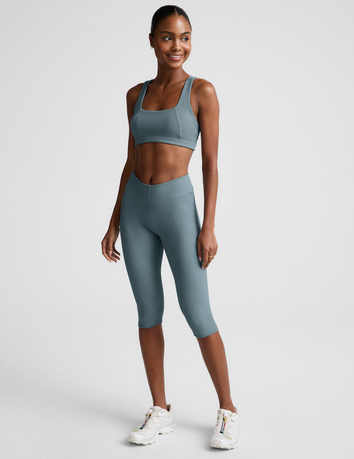 Woman wearing a blue scoop neck bra and leggings against a plain background.