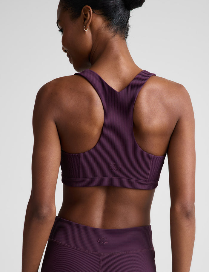 Woman wearing a purple ribbed bra and leggings against a plain background.