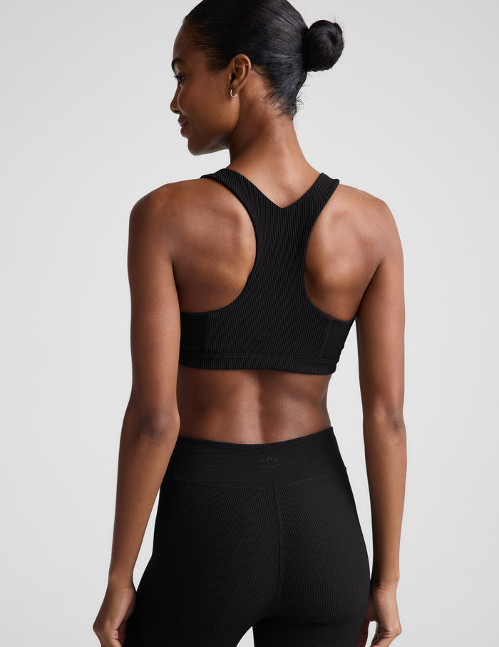 Woman wearing a black ribbed bra and black leggings against a plain background.