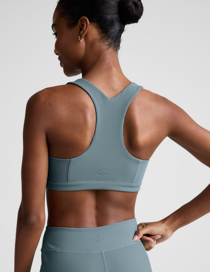 Woman wearing a blue scoop neck bra and leggings against a plain background.