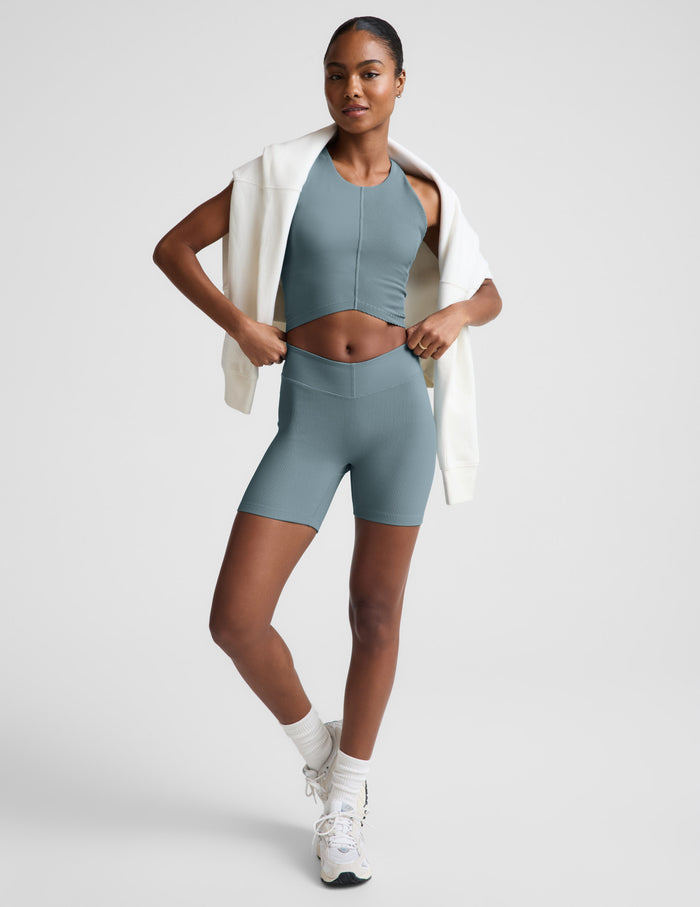 Woman wearing Slate blue Impulse Ribbed V-Waist 5" Biker Short™ paired with a matching crop top and white sweatshirt.