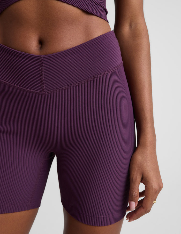 Woman wearing Purple Impulse Ribbed V-Waist 5" Biker Short paired with a matching ribbed crop top.