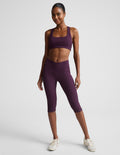 Woman wearing Purple Impulse™ Ribbed V-Waist Pedal Pusher Legging with a matching bra and cream sneakers.