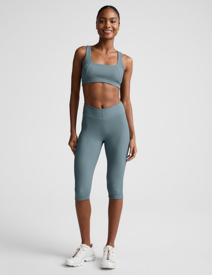 Woman wearing Blue Impulse Ribbed V-Waist Pedal Pusher Legging paired with a matching sports bra and white sneakers.
