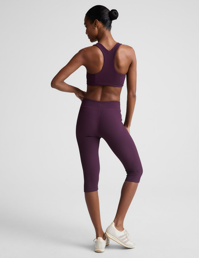 Woman wearing the Purple Impulse™ Ribbed V-Waist Pedal Pusher Legging, paired with a matching bra and cream sneakers. Rear view.