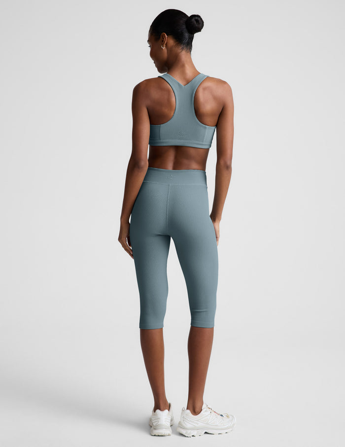 Woman wearing Slate blue Impulse Ribbed V-Waist Pedal Pusher Legging™ with a matching sports bra, rear view.
