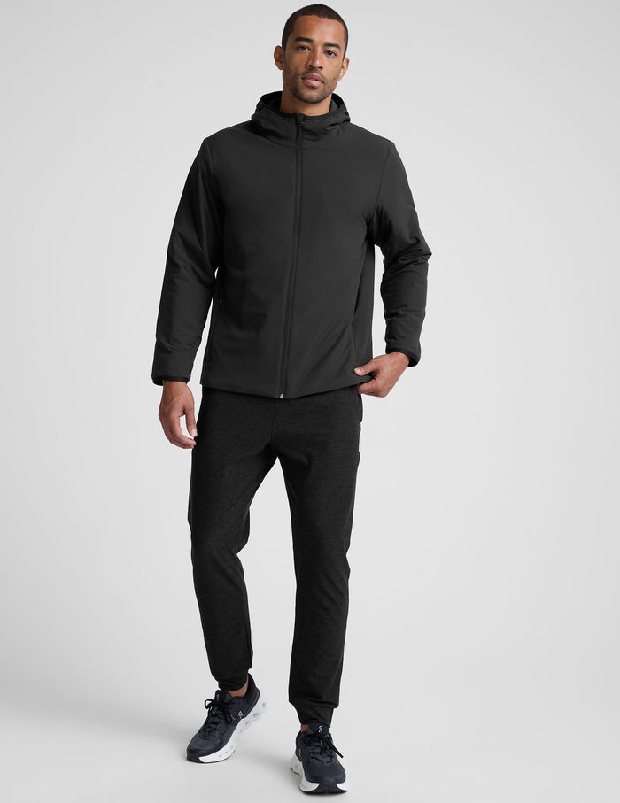 male model wearing a black zip-up jacket with a hood and pockets against a plain background.