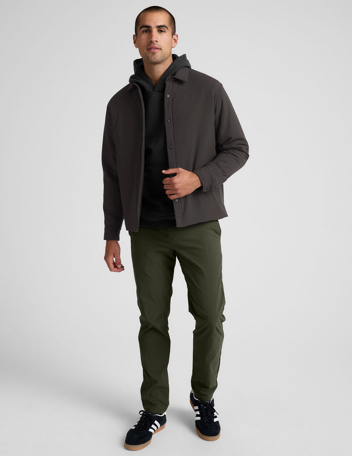 Man wearing a dark jacket, black shirt, green pants, and black sneakers on a white background.