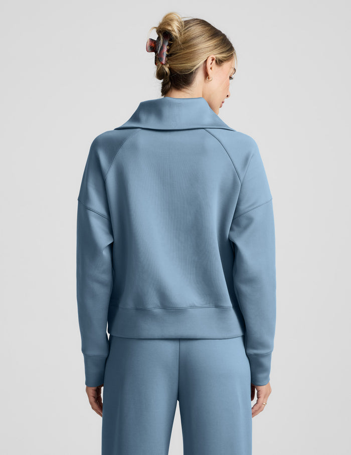 Woman wearing a light blue quarter zip pullover and pants against a plain background.