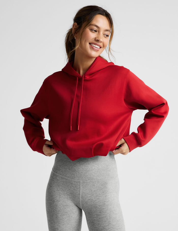 Woman wearing a red hoodie and gray leggings on a light gray background.