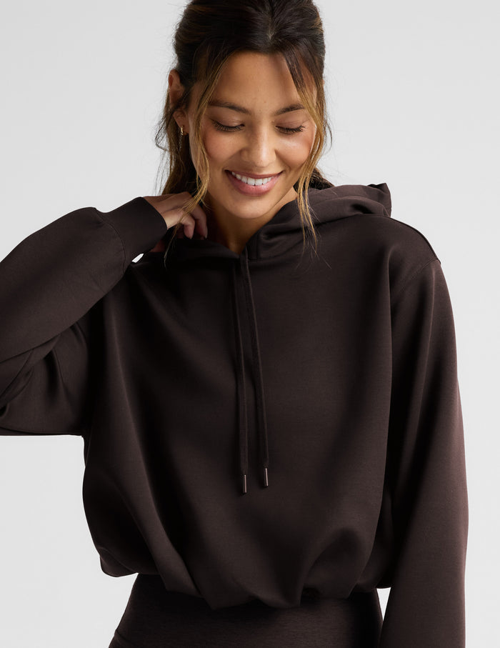Woman wearing a brown hoodie and leggings on a light gray background.