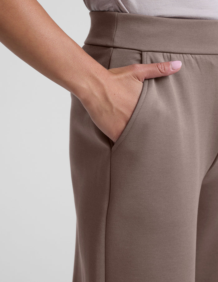 Hand in the slant pocket of the beige In The Flow Wide Leg Pant featuring a smooth, high-rise elastic waistband.