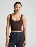 Woman wearing a brown ribbed cropped tank and blue pants against a plain background.