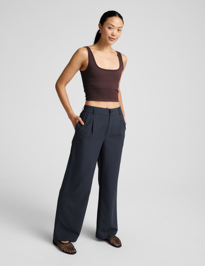 Woman wearing a brown ribbed cropped tank and blue pants against a plain background.