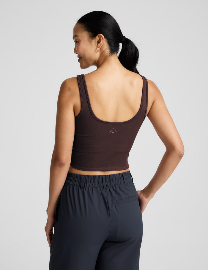 Woman wearing a brown ribbed cropped tank and blue pants against a plain background.