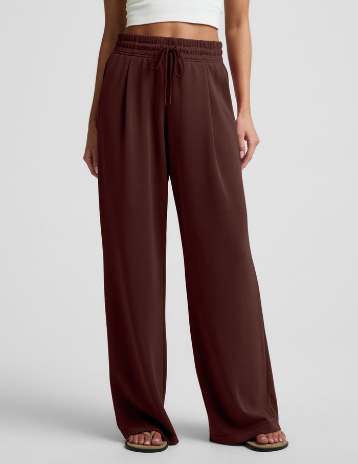 Woman wearing a white cropped tank and brown wide leg pants against a plain background.