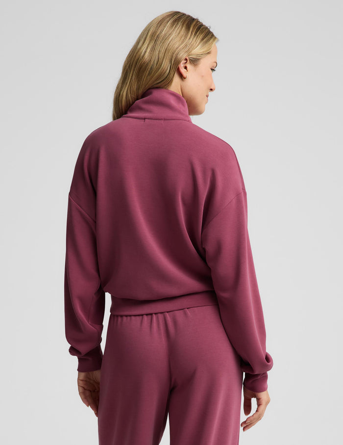 A woman modeling a matching dusty rose half-zip sweatshirt and drawstring sweatpants set against a solid light gray background.