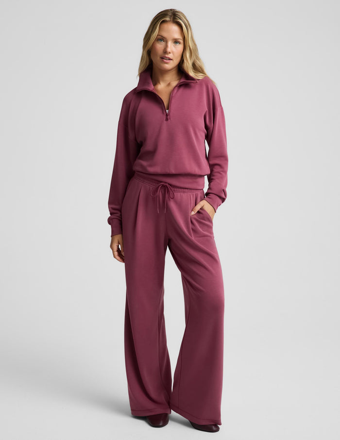 A woman modeling a matching dusty rose half-zip sweatshirt and drawstring sweatpants set against a solid light gray background.