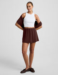 Woman wearing brown Luxe Sandwash™ Skort with a white ribbed tank top and a brown sweater draped over her shoulders.