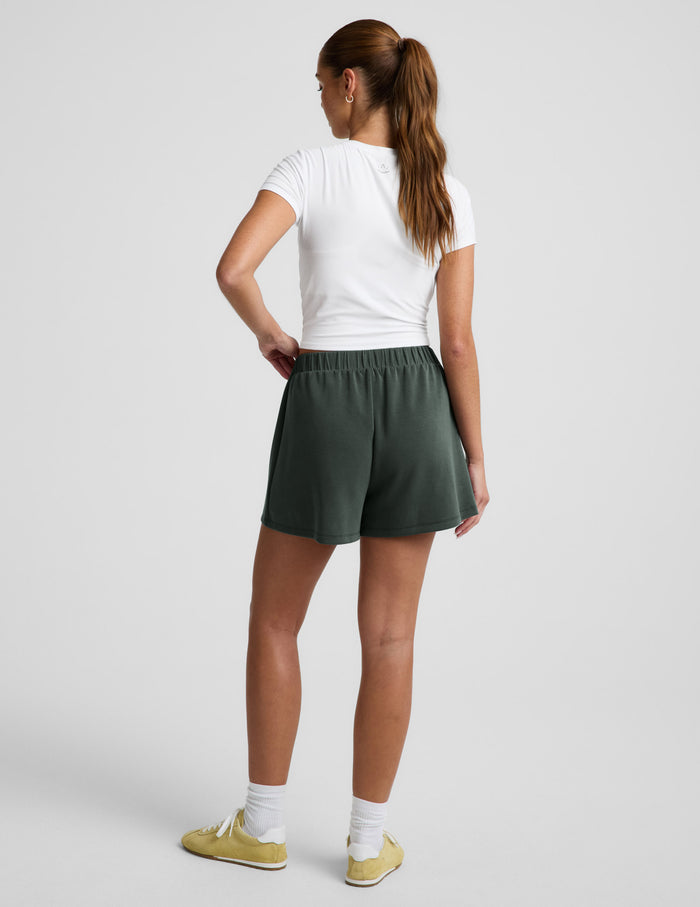 Rear view of woman wearing green Luxe Sandwash Skort™ with a white short-sleeve t-shirt and yellow sneakers.