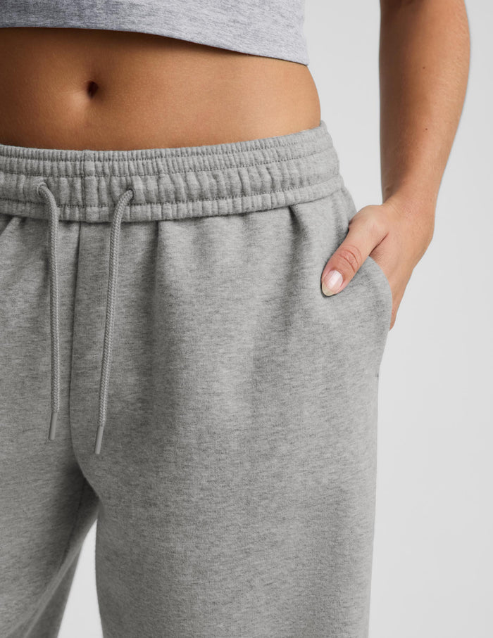 Close-up of a person wearing heather gray sweatpants with an elastic drawstring waistband and side pockets, against a light gray studio background.