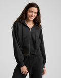 Woman wearing a black fleece zip-up sweatshirt and black sweatpants against a plain background.