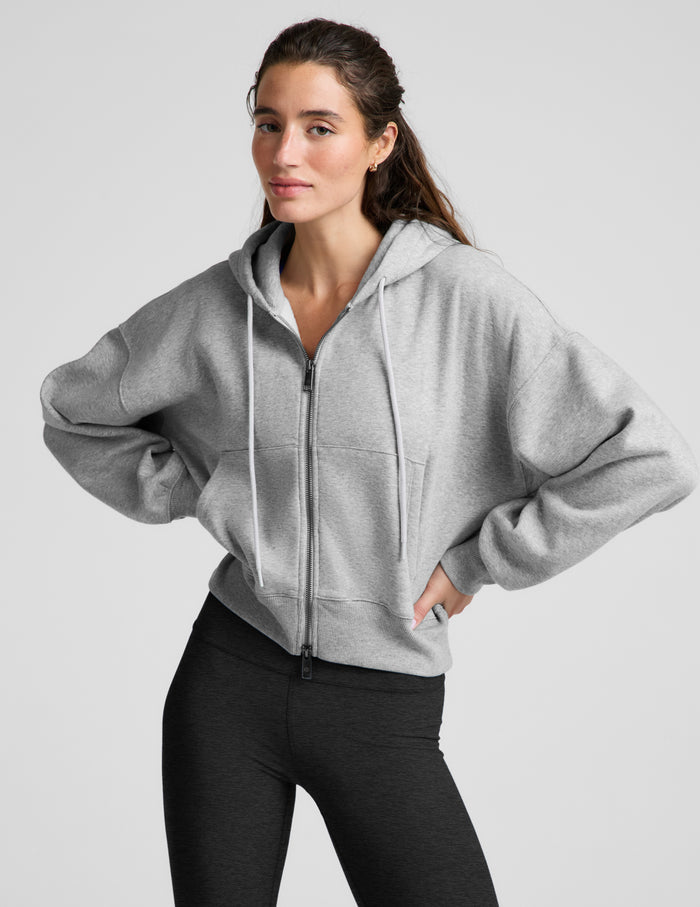 Woman wearing a green zip-up fleece sweatshirt and black leggings against a plain background.