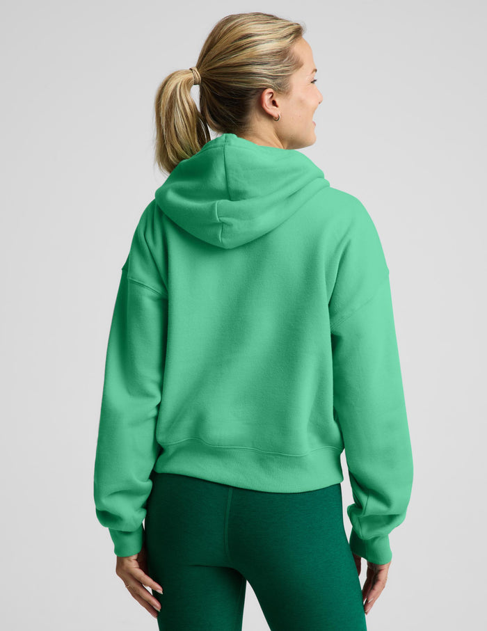 A woman shown from the back wearing a bright green cropped hoodie and matching green leggings against a light gray studio background.