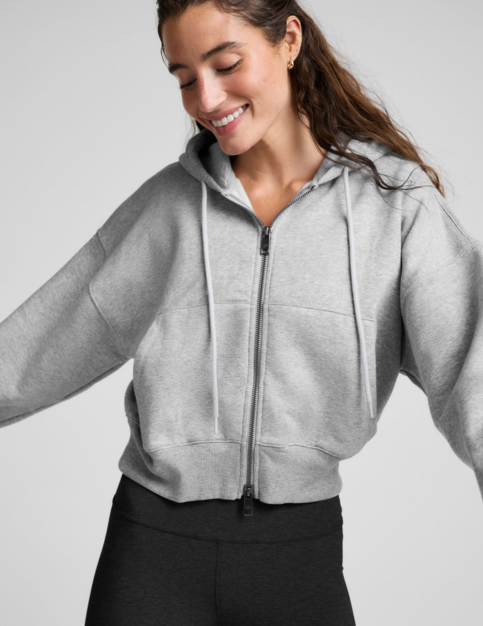Woman wearing a green zip-up fleece sweatshirt and black leggings against a plain background.